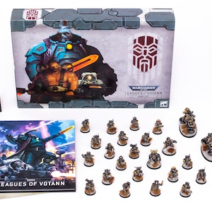 Könnte beinhalten: Warhammer 40.000 Leagues of Votann Start Collecting Box-Set. Die Box enthält eine Vielzahl von Miniaturen, darunter ein Charaktermodell, eine Einheit von Kriegern und eine Einheit von schweren Waffen. Die Box enthält auch ein Regelbuch und einen Satz Würfel.
