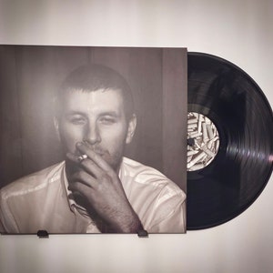 Op de afbeelding: Een zwart-witfoto van een persoon die een sigaret rookt. De foto staat op de hoes van een vinylplaat.