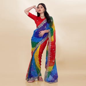 May include: A woman in a colourful saree, featuring a rainbow gradient of colours and silver embroidery. The saree transitions from blue to green, yellow, and red. She is also wearing a red blouse.