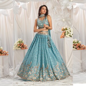 May include: A light blue embroidered lehenga with silver embellishments and a matching sleeveless crop top. The skirt features a floral design and a silver belt.