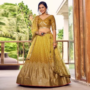 May include: A mustard yellow lehenga choli set featuring a cropped blouse with a V-neckline and half sleeves, paired with a pleated, floor-length skirt adorned with intricate gold embroidery and a matching sheer dupatta with decorative borders.