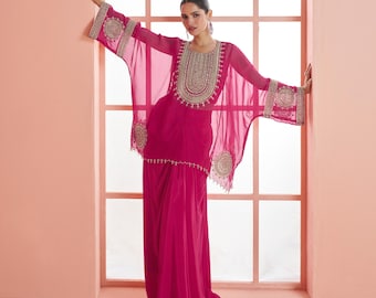 Può includere: Un abito in stile caftano color magenta con ricami dorati intricati intorno allo scollo e sulle maniche. L'abito presenta un rivestimento trasparente e una gonna abbinata. Le maniche sono ampie e fluide e l'abito è lungo.