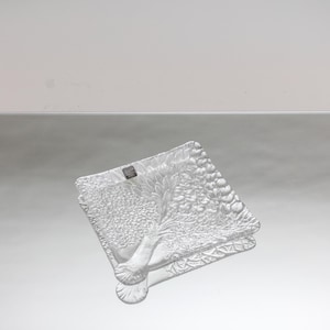 Puede incluir: Un plato de servir de vidrio transparente con un diseño en relieve de un árbol con hojas y ramas. El plato es cuadrado y tiene un borde ligeramente redondeado.