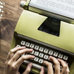 May include: A person types on a vintage green typewriter with a white sheet of paper inserted. The typewriter has a standard keyboard layout with white keys and black lettering. The paper sheet has text on it, but the text is too small to read.