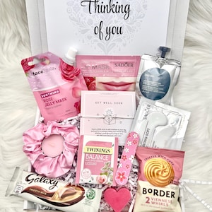 May include: A gift box filled with pink self-care items. Includes a face mask, lip mask, tea, chocolate, a candle, and other treats. The box is decorated with the words "Thinking of you".