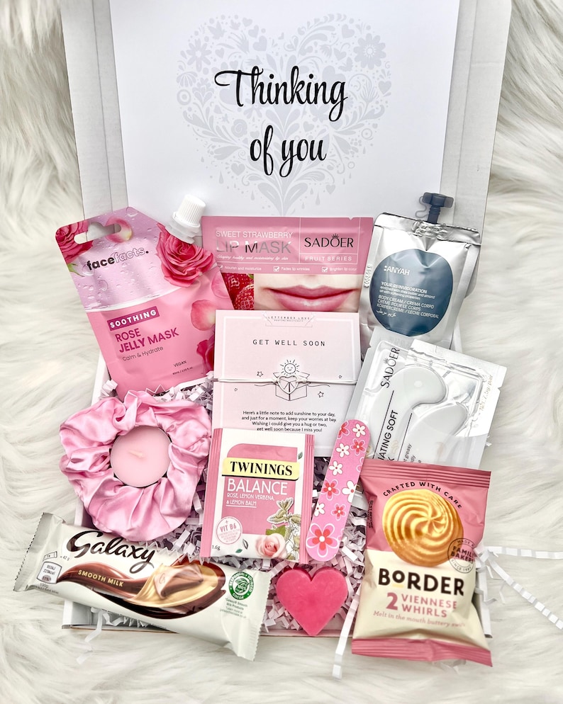 May include: A gift box filled with pink self-care items. Includes a face mask, lip mask, tea, chocolate, a candle, and other treats. The box is decorated with the words "Thinking of you".