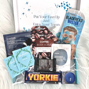 May include: A gift box filled with self-care items, including a coffee body scrub, a blackhead peel-off mask, a blue tea light candle, a chocolate bar, and several small packets of bath and beauty products. The box is decorated with a blue and white patterned paper and the text "Put Your Feet Up And Enjoy Your Treats".