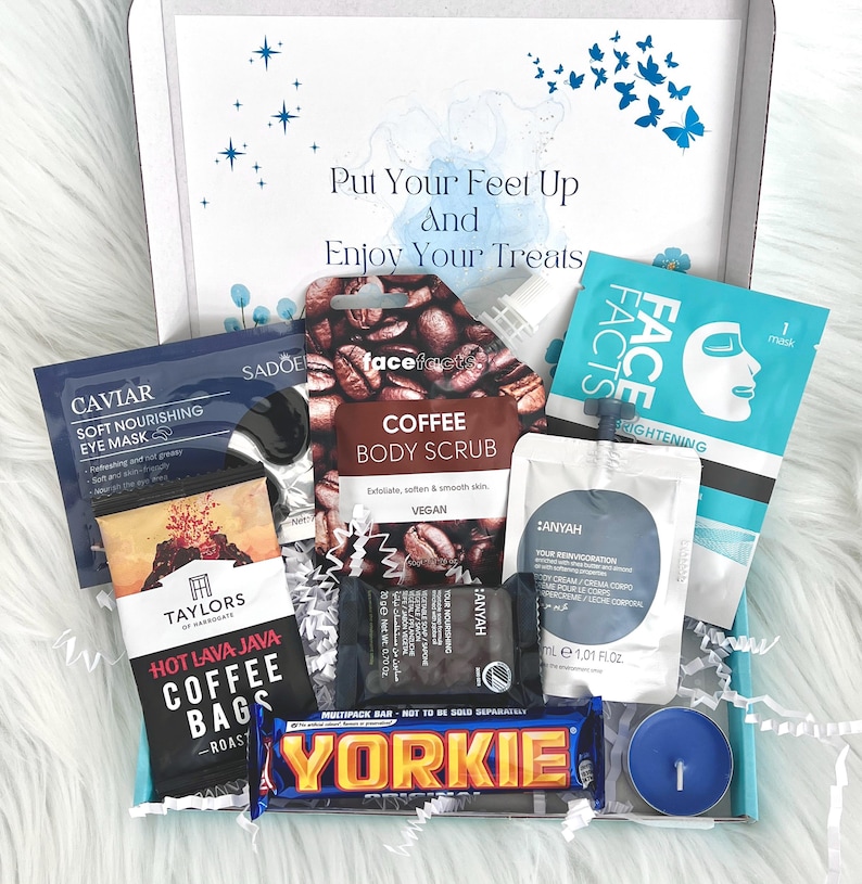 May include: A gift box filled with self-care items, including a coffee body scrub, face mask, eye mask, and a chocolate bar. The box is decorated with a blue and white watercolor background and the text "Put Your Feet Up And Enjoy Your Treats".