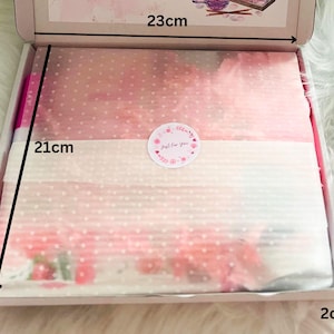 May include: A white cardboard box, 23cm x 21cm x 2cm, containing pink tissue paper with a polka dot pattern. A round sticker with the text "Just For You" is on top of the tissue paper. The box is open, revealing the contents.