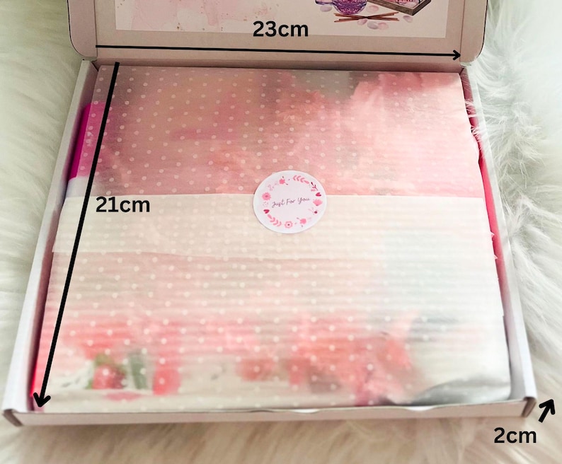May include: A white cardboard box, 23cm x 21cm x 2cm, containing pink tissue paper with a polka dot pattern. A round sticker with the text "Just For You" is on top of the tissue paper. The box is open, revealing the contents.
