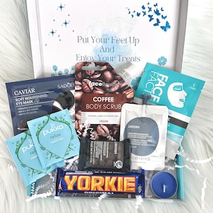 May include: A gift box filled with self-care items, including a coffee body scrub, face mask, eye mask, tea bags, a chocolate bar, and a candle. The box is decorated with a blue and white watercolor design and the text "Put Your Feet Up And Enjoy Your Treats".