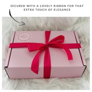 May include: A pink gift box with a red ribbon tied in a bow. The box has a sticker with the words "Pretty Blossom Gifts" on it.