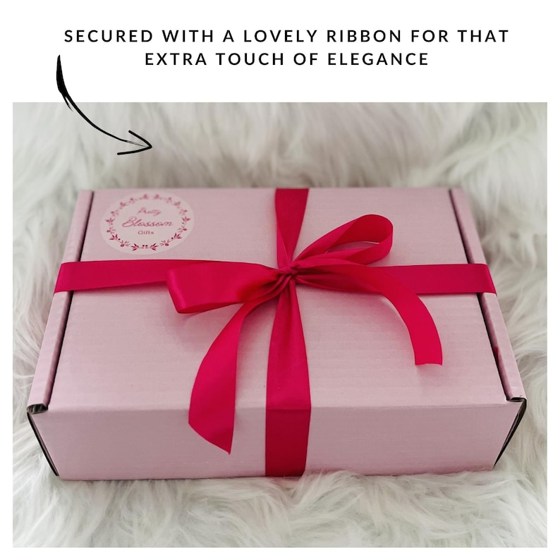 May include: A pink gift box with a red ribbon tied in a bow. The box has a sticker with the words "Pretty Blossom Gifts" on it.