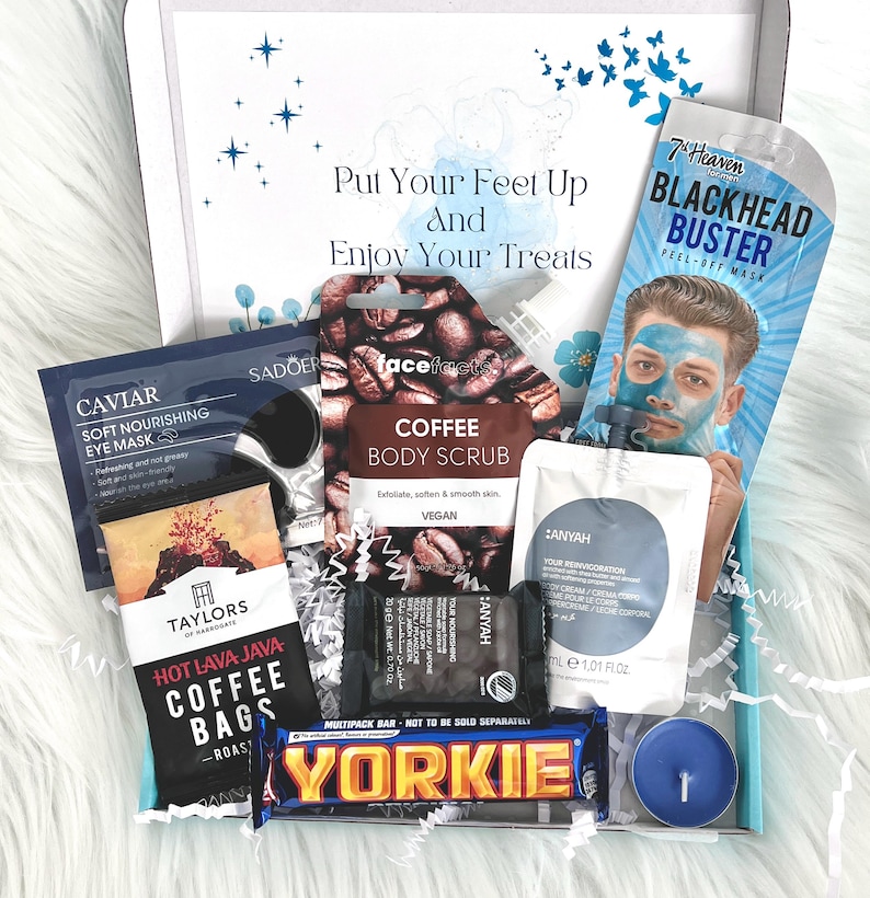 May include: A gift box filled with self-care items, including a coffee body scrub, a blackhead buster peel-off mask, a chocolate bar, and a candle. The box is decorated with blue butterflies and stars.