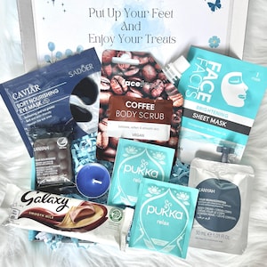 May include: A gift box filled with self-care items. Includes a coffee body scrub, eye mask, face sheet mask, chocolate bar, tea sachets, a candle, and body cream. The box has the text "Put Up Your Feet and Enjoy Your Treats".