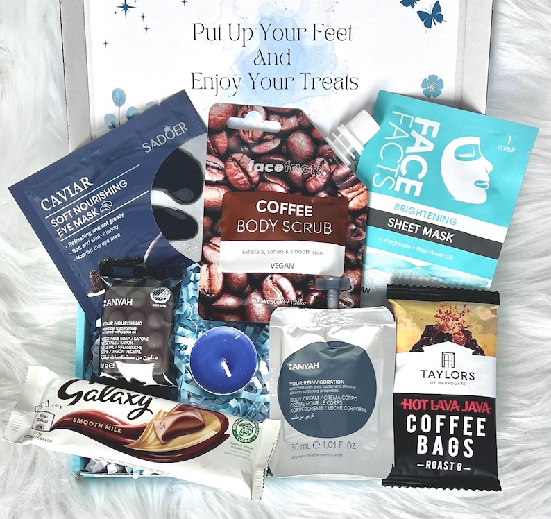 May include: A gift box filled with self-care products. Includes a coffee body scrub, eye mask, sheet mask, body cream, coffee bags, a Galaxy chocolate bar, and a blue candle. The box has the text "Put Up Your Feet And Enjoy Your Treats".