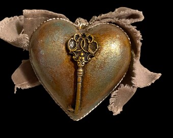 May include: A heart-shaped ornament with a metallic finish in shades of green, brown, and gold. A decorative key is attached to the ornament.