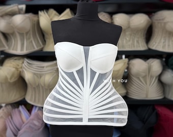 May include: A white strapless corset top featuring structured cups and a sheer mesh bodice with vertical and horizontal white boning strips. The garment displays the text WITH YOU printed in small white letters on the front panel.