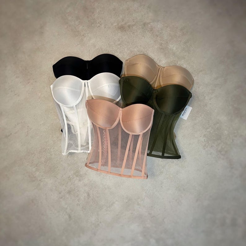 May include: Four strapless mesh corsets in different colors: black, white, nude, and green. The corsets are made of a sheer mesh fabric with a satin lining. The corsets have a boned structure and a hook-and-eye closure in the back.