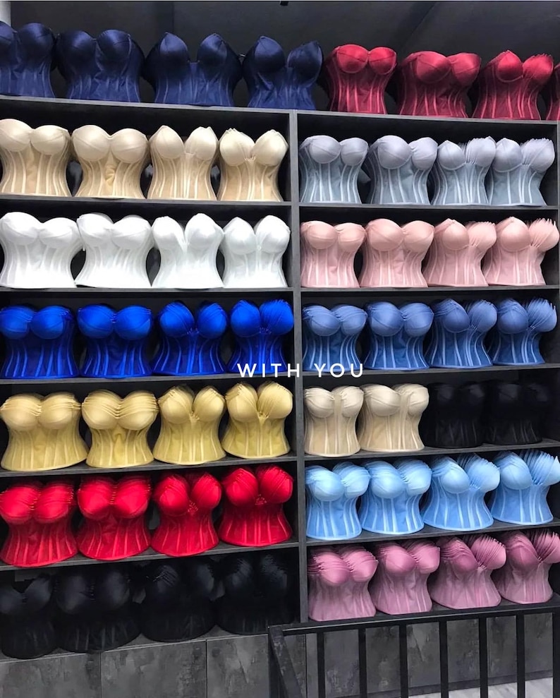 May include: A collection of strapless corset tops in various colors including red, blue, white, black, yellow, and pink, arranged on shelves. The text "WITH YOU" is visible in the center of the display among the rows of garments.