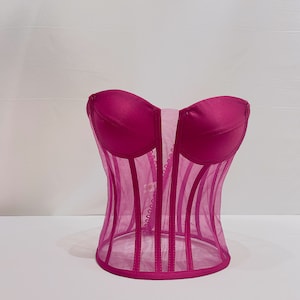 Pu&ograve; includere: Un corpetto rosa in satin e rete con scollo a cuore e dettagli di stecche.