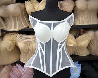 May include: A white corset top featuring structured cups and sheer mesh panels with vertical white piping. The garment has an off-the-shoulder neckline and a pointed hemline. The text WITH YOU is printed in white on the front mesh panel.