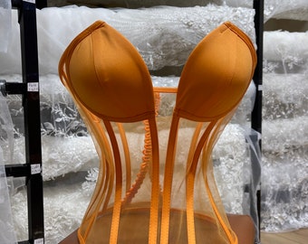 May include: A bright orange mesh corset with a satin lining and boning. The corset has a sweetheart neckline and is designed to cinch the waist.