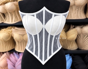 May include: A white strapless corset top featuring sheer mesh panels and opaque molded cups. The garment has vertical boning channels and a pointed hemline. The text "WITH YOU" is printed in white on the right side of the bodice.