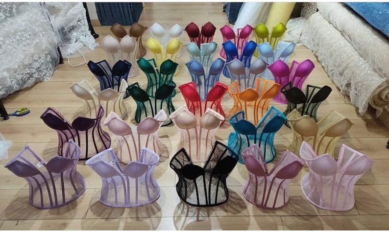 May include: A collection of 20 different colored mesh corsets with boning. The corsets are displayed on a wooden floor.