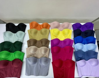 May include: A collection of 15 strapless bustiers in various colors, including black, green, red, blue, yellow, and purple. The bustiers are arranged in rows on a white surface.