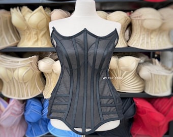 May include: A black corset top featuring sheer mesh panels and structured vertical boning. The garment has a sweetheart neckline and horizontal strap details at the waist. The text "WITH YOU" is printed in white on the center of the bodice.
