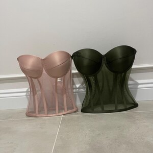 May include: Two strapless mesh corsets, one in pink and one in green. Both corsets have a satin top and a mesh bottom with vertical lines.