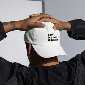 May include: White baseball cap with black text that reads "beef, barbells & bitcoin."
