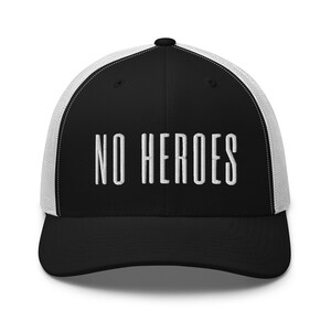 Könnte beinhalten: Eine schwarze und weiße Trucker-Kappe mit weißem Netzrücken. Die Vorderseite der Kappe ist mit dem Text "NO HEROES" in Weiß bestickt.