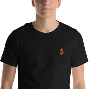 Könnte beinhalten: Schwarzes T-Shirt mit einem kleinen orangefarbenen gestickten Logo einer Fackel mit einem "B" darauf.