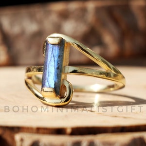 May include: Gold ring with a blue labradorite gemstone set in a simple, modern design. The ring has a delicate, open band with a rectangular stone.