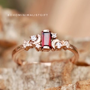 May include: A rose gold ring with a red gemstone and small white gemstones set in a crescent moon and star design.