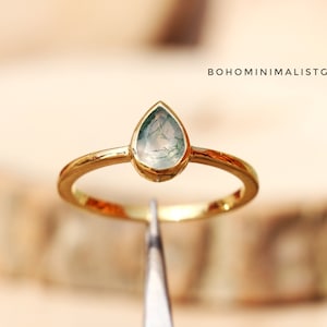 May include: A gold ring with a teardrop-shaped green agate stone. The ring is on a wooden surface.