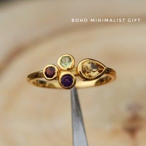 Può includere: Anello in oro con cinque pietre preziose colorate. L'anello presenta una pietra gialla a forma di pera, una pietra verde rotonda, una pietra viola rotonda e due pietre rosse rotonde.