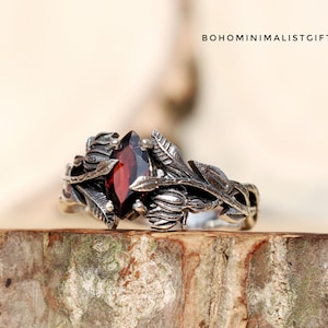 Könnte beinhalten: Ein silberner Ring mit einem roten Edelstein, der in einem floralen Design gefasst ist. Der Ring liegt auf einer Holzoberfläche.