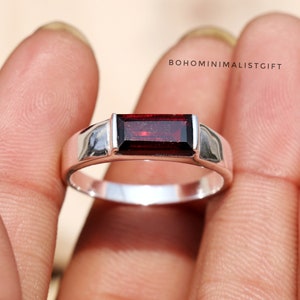 Könnte beinhalten: Ein silberner Ring mit einem rechteckigen roten Edelstein. Der Ring ist in einer einfachen Band mit polierter Oberfläche gefasst. BOHOMINIMALISTGIFT ist im Hintergrund gedruckt.