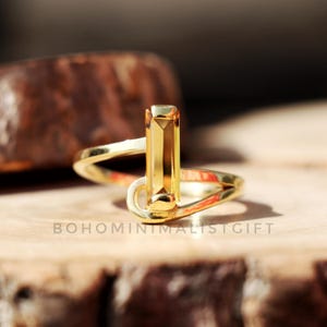 Peut inclure: Une bague en or avec une pierre précieuse rectangulaire, facetée et jaune. La bague a un design simple et moderne.