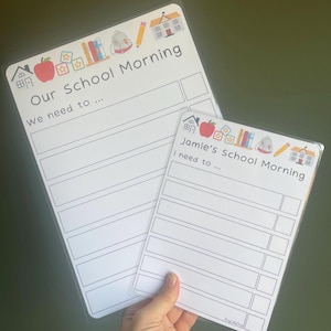May include: Two white dry-erase boards with colourful illustrations of school supplies and a house. The top board says "Our School Morning" and has the text "We need to..." The bottom board says "Jamie's School Morning" and has the text "I need to..."