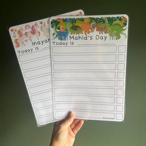 May include: Two laminated daily schedule charts with white backgrounds. One features colourful unicorns and rainbows with the text Inayah Today is. The other features various green, orange, and brown dinosaurs with the text Mahid's Day Today is.