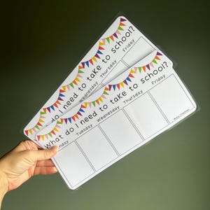 May include: Two laminated white rectangular charts titled What do I need to take to school? featuring a colorful bunting banner at the top. The charts are divided into columns for Monday through Friday with blank spaces for writing tasks.