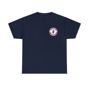 May include: A navy blue t-shirt with a red, white, and blue embroidered patch. The patch features a diamond shape with a lightning bolt and the text "DISTRICT COUNCIL 12 BATTERY PARK EMERGENCY SERVICE"