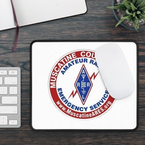 May include: A white mouse pad with a black border. The center of the mouse pad features a red, white, and blue logo with the text "Muscatine County Amateur Radio Emergency Service" and the website "www.MuscatineARES.org".