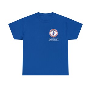 May include: Royal blue short-sleeved t-shirt with a white embroidered logo of the "Midland County Fire Department Emergency Services" emblem. The text "Emergency Communications" is also embroidered in white below the logo.
