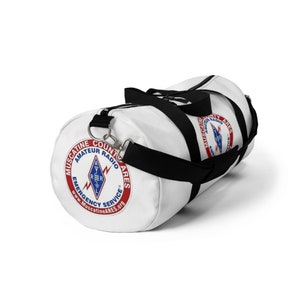 May include: White canvas duffel bag with a black zipper and black straps. The bag has a red, white, and blue logo that says "Muscatine County Amateur Radio ARES Emergency Service" and "www.MuscatineARES.org".
