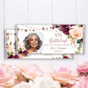 May include: A white chocolate bar wrapper with a floral design in shades of pink, burgundy, and green. The wrapper features a photo of a woman and the text "80th Birthday! thank you for sharing my special day Love. Veronica 08/25/20YY 08/25/20YY".